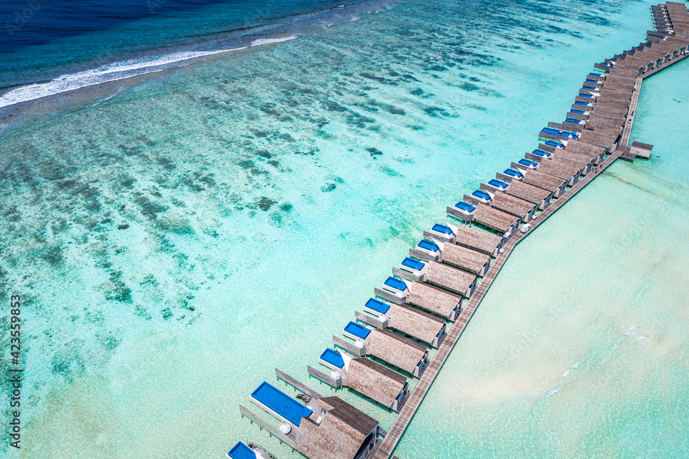 Luxury overwater villas with amazing coral reef, blue ocean lagoon, white sandy beach at famous destination, aerial scenic as Bora Bora, Tahiti, French Polynesia or Maldives islands. Summer vacation