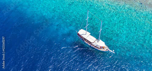 Sailing yacht in Maldives islands. Aerial drone view of white sailboat anchored, crystal clear turquoise ocean. Summer recreational sport activity, snorkeling, diving. Amazing aerial sea nature banner © icemanphotos