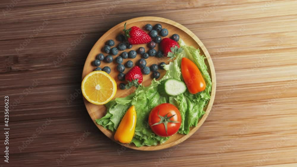 Variety of color fruits and berries and vegetables with greens are rotating on the plate. Healthy food clean eating selection. Variety of color fruits and berries and vegetables with greens are rotating on the plate. Healthy food clean eating selection.