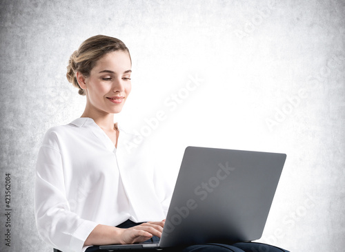 Young businesswoman with laptop, mockup empty wall
