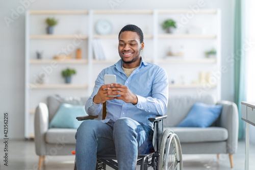 Disabled black man in wheelchair using smartphone, browsing web or watching movie at home