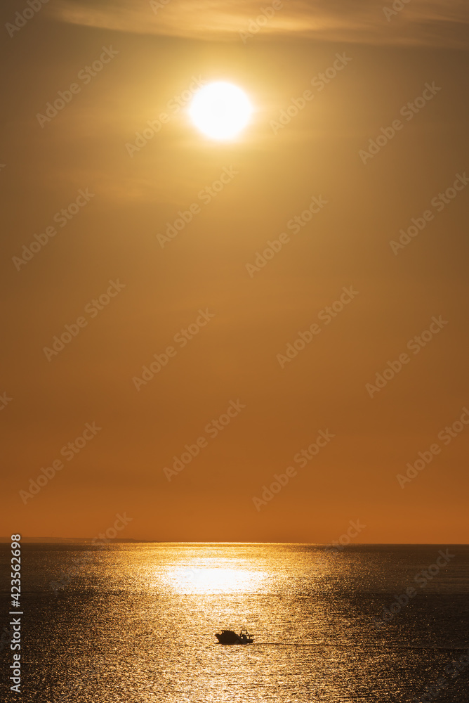 Landscape with the sun reflected in the sea and the silhouette of a fishing boat on the reflection.