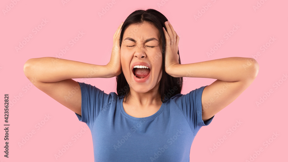 Angry asian woman covering her ears with hands and screaming Angry asian woman covering her ears with hands and screaming