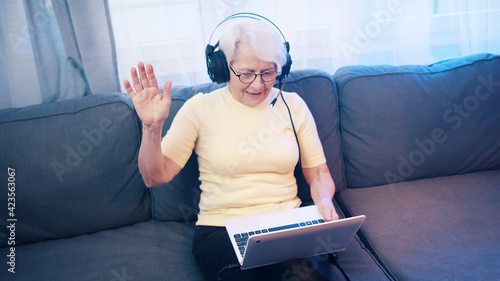 Elderly woman with headset having video call with family and waving to camera. Old people and technology. High quality photo photo