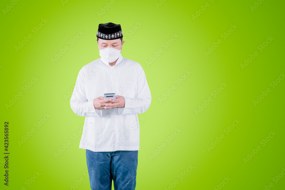 Muslim man in face mask using cellphone on studio
