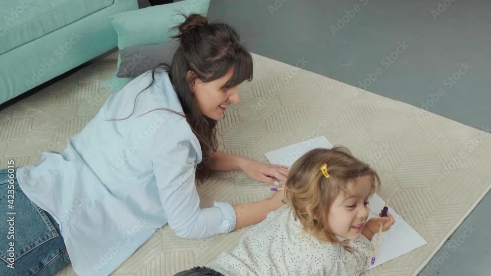 Mom and daughter lying on carpet on the floor, drawing on paper together. Mom and daughter lying on carpet on the floor, drawing on paper together.