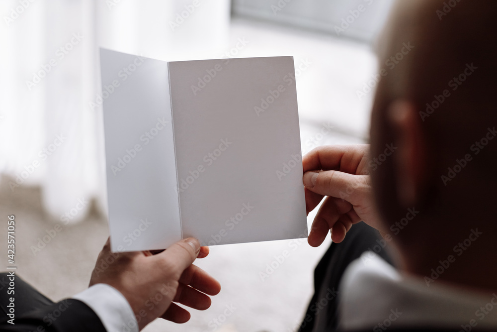 the groom holds an envelope with a letter from the bride. man is reading and sitting in the chair near the window. A letter for the groom. declaration of love. mock up place the groom holds an envelope with a letter from the bride. man is reading and sitting in the chair near the window. A letter for the groom. declaration of love. mock up place