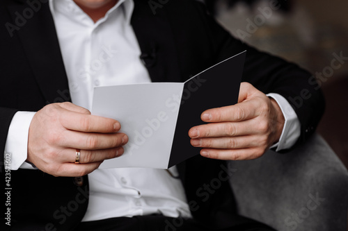 the groom holds an envelope with a letter from the bride. man is reading and sitting in the chair near the window. A letter for the groom. declaration of love.