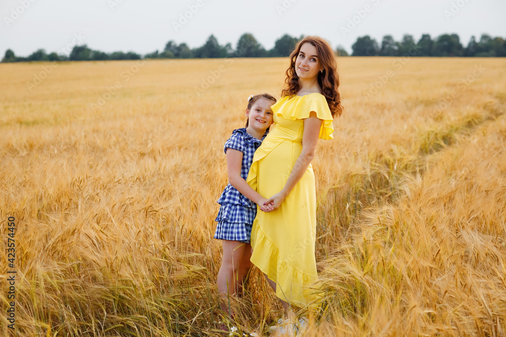 Pregnant mother and daughter in a wheat field at sunset. Gentle family hugs of mother and child in nature. Pregnant mother and daughter in a wheat field at sunset. Gentle family hugs of mother and child in nature.