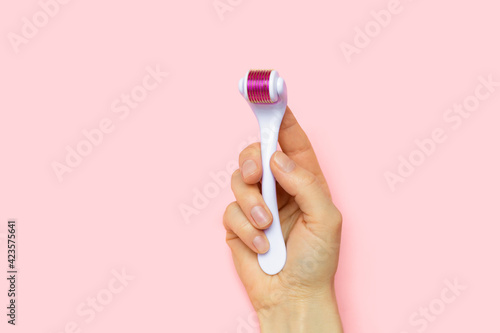 dermaroller, mesoroller, microneedling. cosmetic tool with micro needles in female hand on pink background for skin care of face, neck, hands, fight against cellulite. copy space, place for text