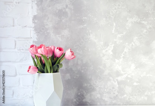Fototapeta Naklejka Na Ścianę i Meble -  Pink tulip bouquet in vase on white table on white brick wall and bright concrete background. Copy space for text.