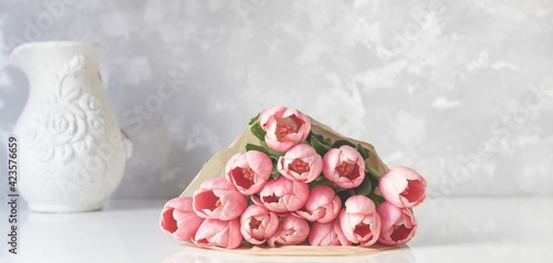 Bouquet of fresh pink tulips on white table with vase on the background. Copy space for text.