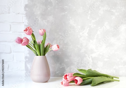 Pink tulip bouquet in vase on white table on white brick wall and bright concrete background. Copy space for text.