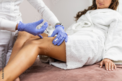 Attractive young woman is getting a rejuvenating injections in her legs by beautician expert.