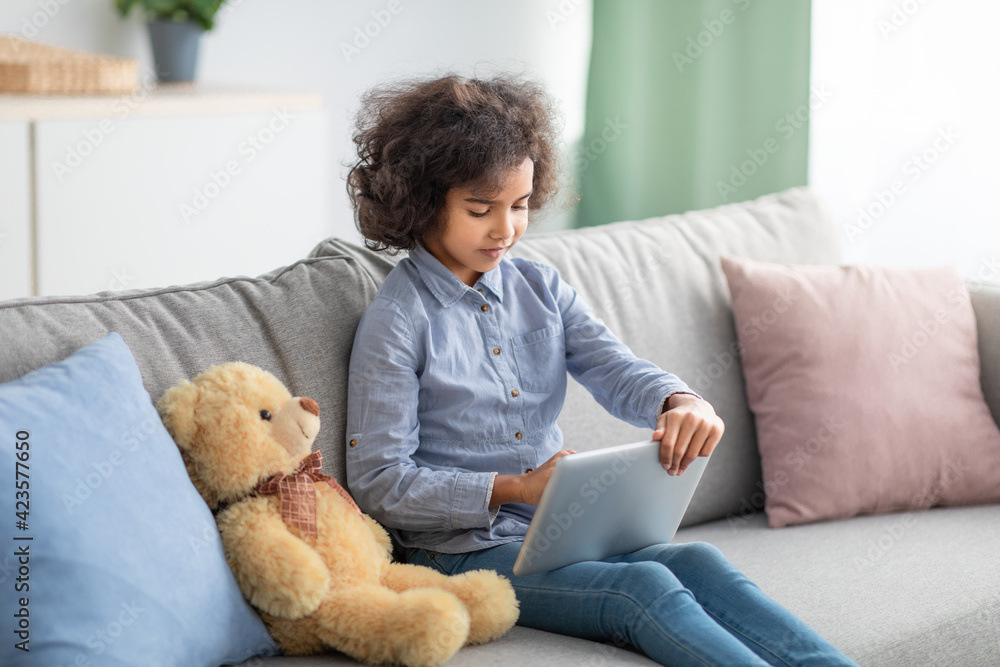 Afro girl using digital tablet, sitting on sofa Afro girl using digital tablet, sitting on sofa