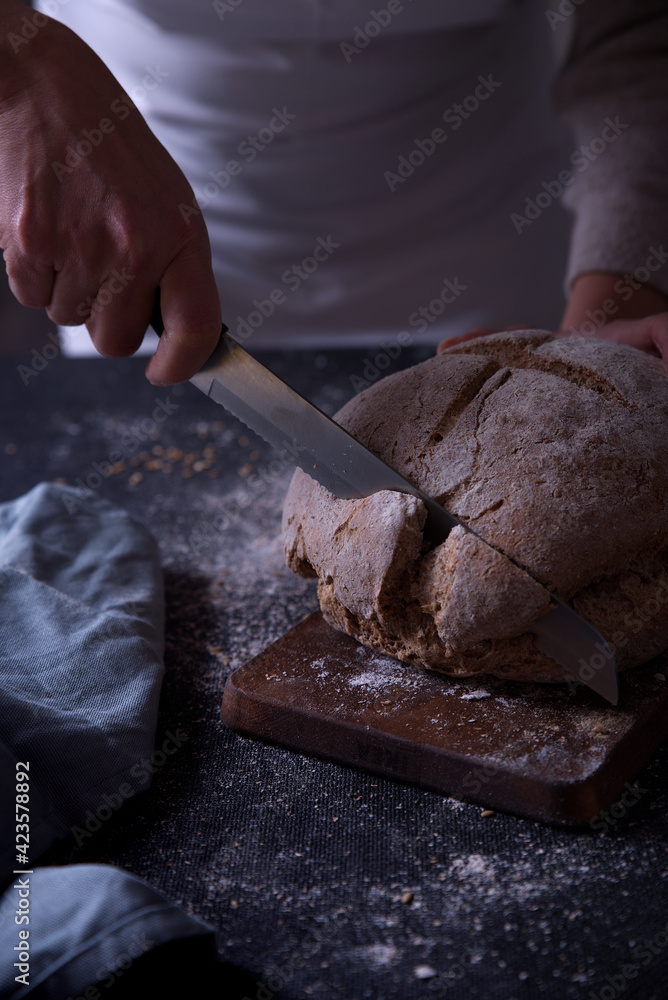 Hands slicing fresh bread, on dark background. Hands slicing fresh bread, on dark background.