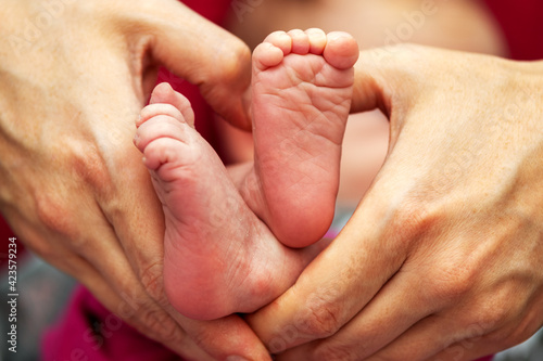 Eine junge Mutter formt mit Ihren Händen ein Herz indessen Mitte sich die Füße Ihres neugeborenen Babys befinden