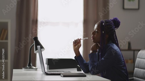 afro-american female student is preparing to exam, learning at home with laptop, sitting at table and thinking or reflecting photo
