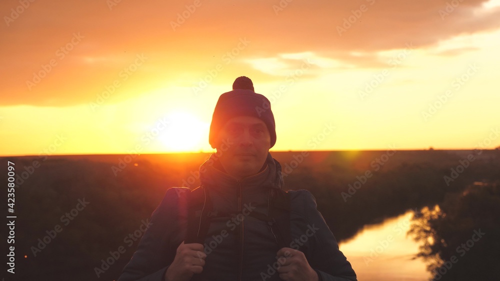 A man traveler with a backpack on his shoulders walks along a high mountain at sunset in the sky, overcome obstacles and seek adventures, a tourist trip for the hardy and strong, close-up