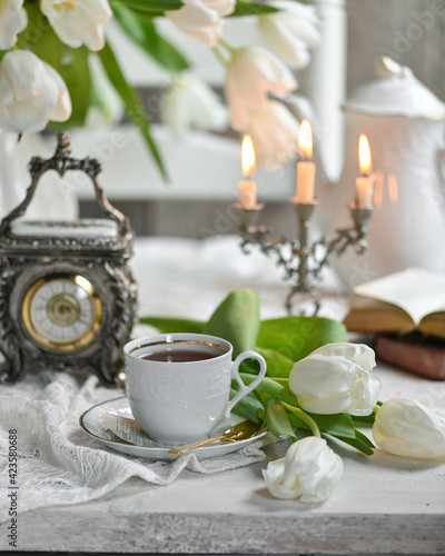 A bouquet witte tulips in a vase, a white alarm clock en kopje koffie op witte tafel. traditional English tea, high tea 