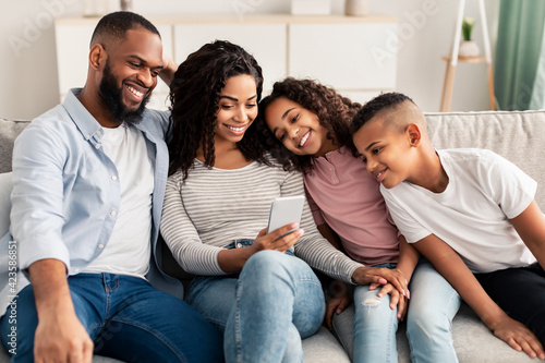 Happy african american family holding and using smartphone