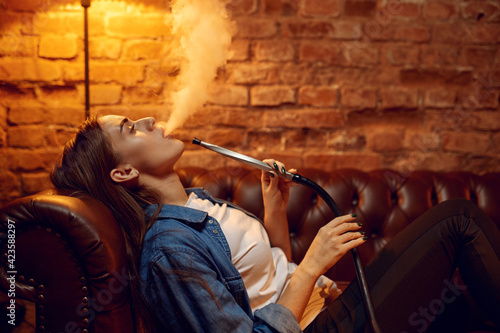 Young woman smokes on sofa in hookah bar