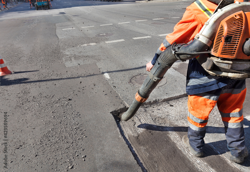 A worker cleans the road section being repaired with an industrial vacuum cleaner. Partial repair of the asphalt road.