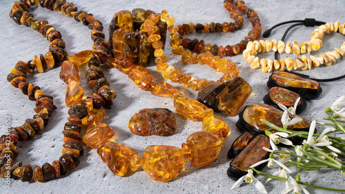 Variety of beautiful yellow and orange amber jewelry on a gray background. Isolated sparkling amber necklaces and leather pendant amulet with snowdrops. Ancient Slavic culture.