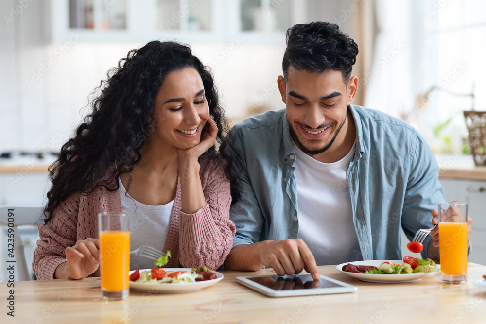 Online Shopping. Happy Arab Spouses Using Digital Tablet During Breakfast In Kitchen