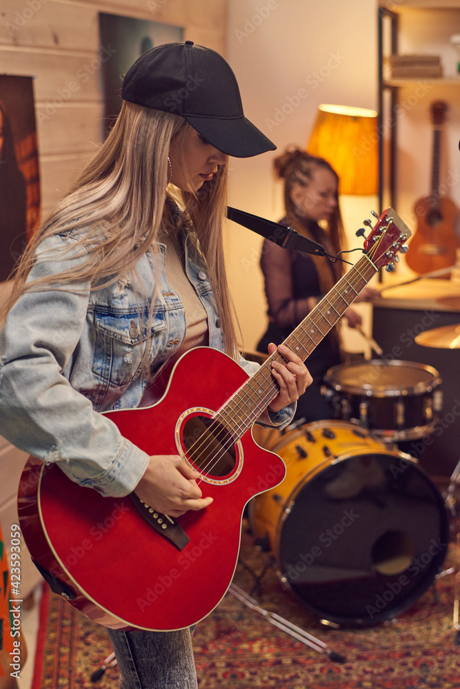 Fototapeta premium Young female guitarist playing electric guitar with her musical group in studio