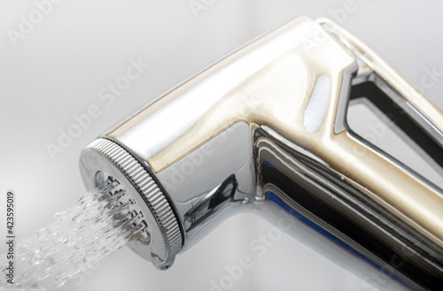 A chrome bidet shower spraying water, close up. The head of the toilet bidet. photo