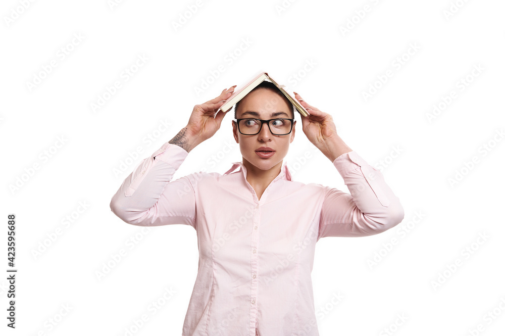 Surprised businesswoman looking to the side and putting pink book or diary on her head like a house isolated on white background Surprised businesswoman looking to the side and putting pink book or diary on her head like a house isolated on white background