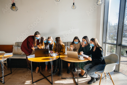 A group of girls in masks sit in a cafe and work on laptops. Teaching students.