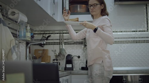 Young woman wearing pajamas take a sandwich out of microwave on a table. Isolated woman having breakfast due to workinig from home photo