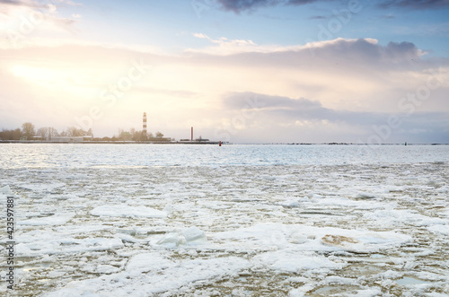 Baltic sea shore at sunset. Lighthouse in the background. Snow, ice fragment on the water. Colorful sunset clouds, golden sunlight. Gulf of Riga, Latvia. Climate change concept. Symbol of hope, peace photo