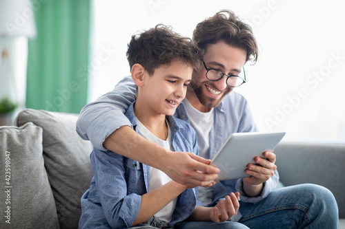 Weekend family leisure. Happy father and son using tablet computer, browsing internet online at home