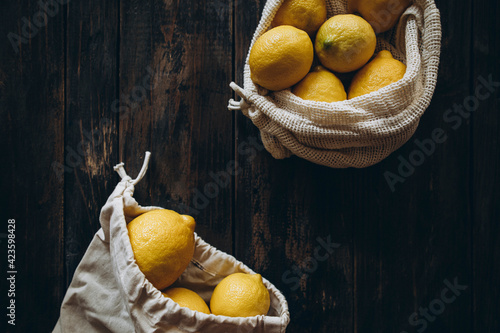 lemons in an eco bag on a wooden table. knitted bags without plastic with lemons. organic lemons on wood background. copy space lemons and space for text
 photo