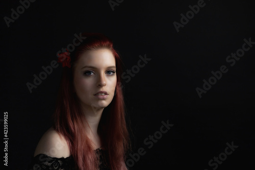Low key portrait of beautiful young woman with red rose in her red hair. Horizontally. 