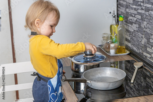 Cute little boy is laying a glass lid on the pan in the kitchen. Horizontally. 