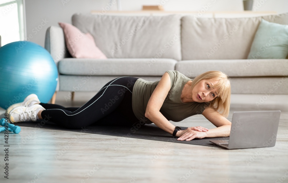 Tired senior woman lying on sports mat near laptop computer, needing break from domestic online training, copy space Tired senior woman lying on sports mat near laptop computer, needing break from domestic online training, copy space