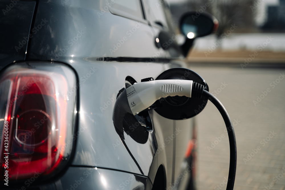 A compact black electric car charges up in a parking lot to maintain the environment. A compact black electric car charges up in a parking lot to maintain the environment.