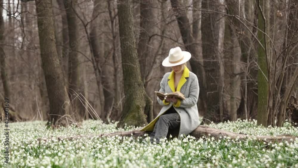 stylish girl in gray coat with a book in snowdrops meadow in forest stylish girl in gray coat with a book in snowdrops meadow in forest