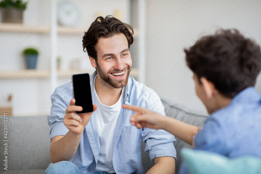 Handsome father showing smartphone with blank black screen to his son, place for mockup