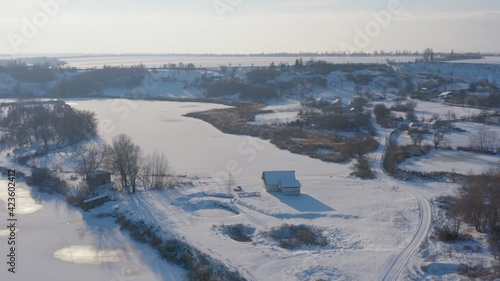 winter fishing house after snowfall. spectacular and very colorful winter sunset in the village. cozy house on the shore of a winter lake - Aerial Flight © Dmytro