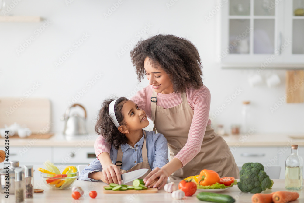Cheerful black woman teaching girl how to prepare salad Cheerful black woman teaching girl how to prepare salad