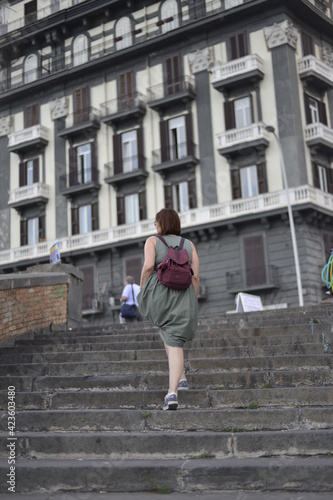 Photo from back of young woman  wearing summer dress and bag walking up stairs in old town   © Anastasia