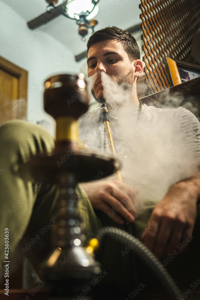 Young handsome guy smoking hookah alone closeup. Hookah and sparks from coals. Shisha, spark, hookah sparks. Young man smokes a fragrant oriental hookah. Young handsome guy smoking hookah alone closeup. Hookah and sparks from coals. Shisha, spark, hookah sparks. Young man smokes a fragrant oriental hookah.