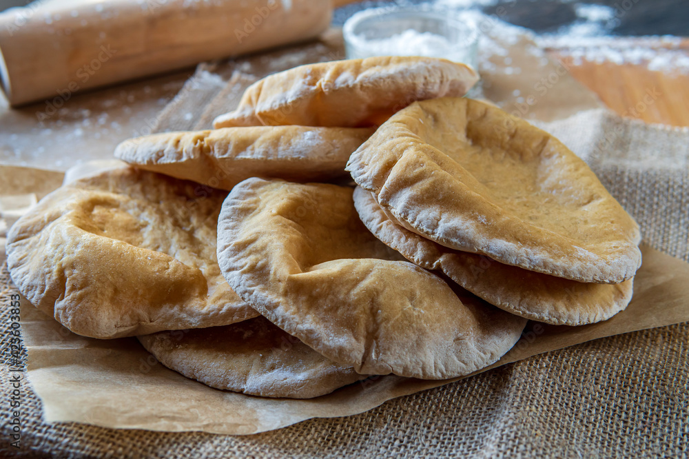 Stack of homemade, fluffy, pita bread. Freshly baked gluten-free pita bread on a rustic cloth, hot from the oven. Round flatbread that can be stuffed with food. Rolling pin and flour in the background