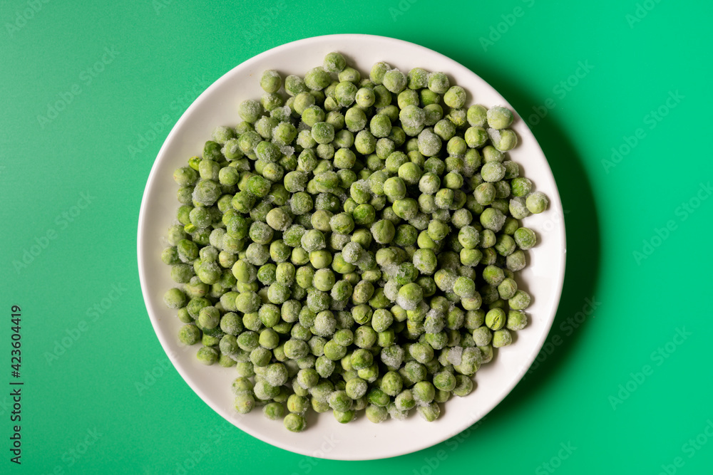 Frozen green peas in a bowl on green background. Frozen green peas in a bowl on green background.