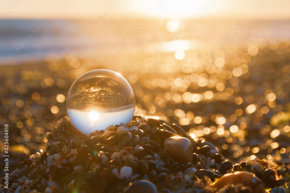 Glass round ball on the beach reflects the sea in summer at sunset